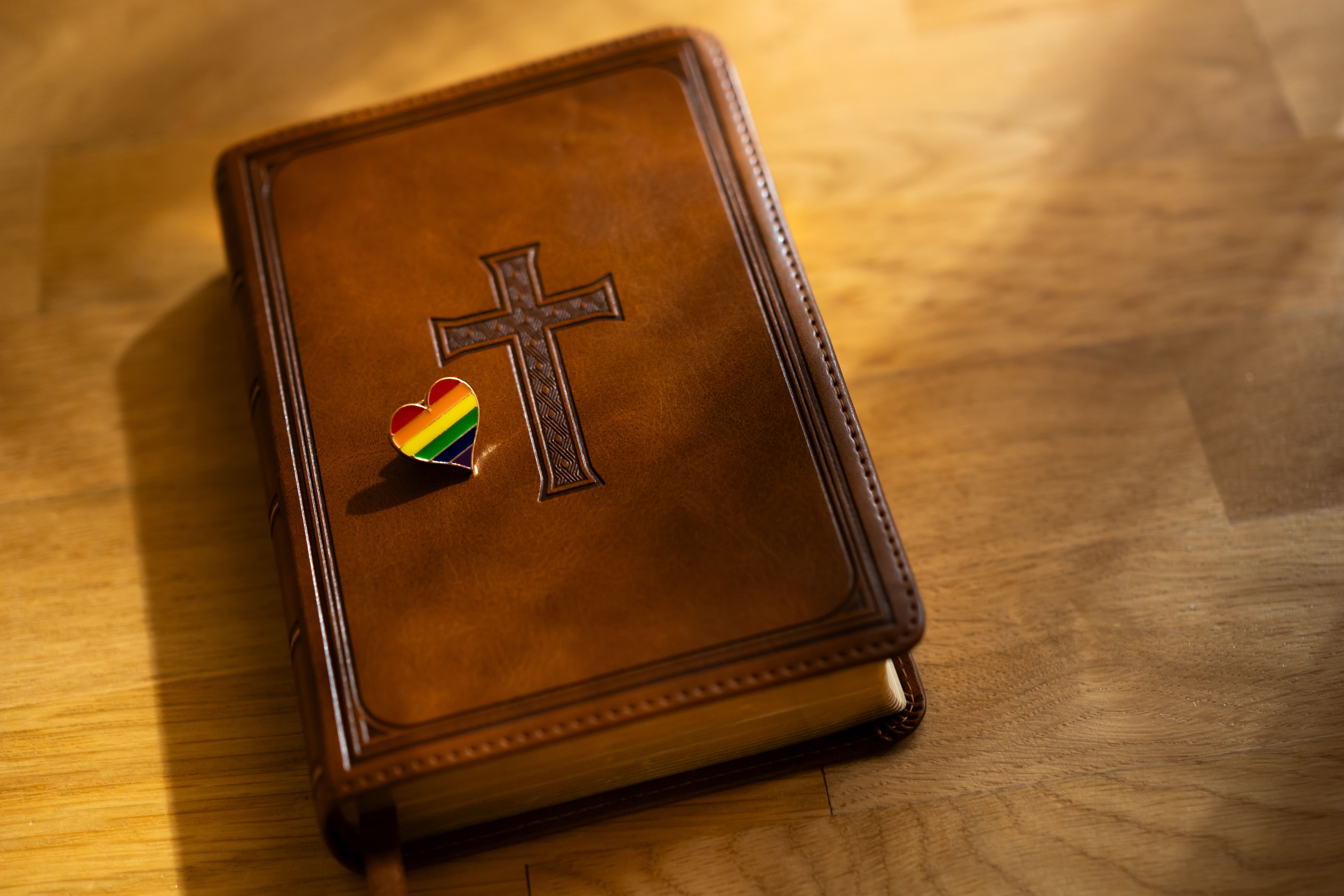 Buch mit Kreuz am Umschlag und Herz in Regenbogenfarben